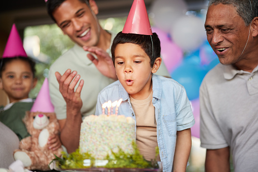 Boy, birthday party and blow candles with cake, celebration and support with applause, hat and happy in family home. Child, flame and wish with congratulations, food and dessert with gift at event