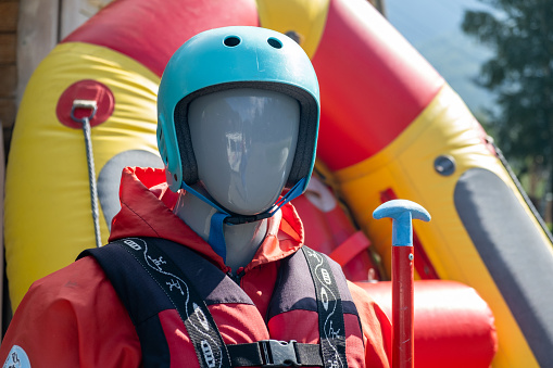 A mannequin in a red life jacket next to an inflatable boat as an advertisement for rafting or boating on the river in tourist places.