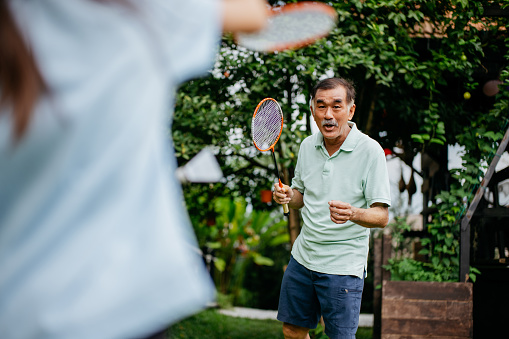 An Asian Chinese senior man playing badminton with his granddaughter in the park