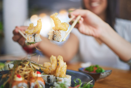 Chopsticks, girl friends hands and shrimp sushi at a table  with Japanese cuisine food at restaurant. Young women, eating and tempura prawn with fish for lunch and meal on a plate with a smile
