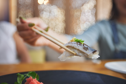 Food, hand and eating sushi with chopsticks at restaurant for nutrition and health. Closeup of a hungry person with wooden sticks for dining, Japanese culture and cuisine with creativity on fish