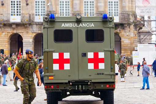 Military Ambulance in an exhibition, rear view of  Ambulance truck with Red Cross painted parked in Obradoiro town square, Santiago de Compostela, Galicia, Spain. Soldier walking by and group of people in the foreground.