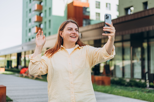 Laughing young woman taking selfie on city background. Happy 30s businesswoman smiling and using smart phone