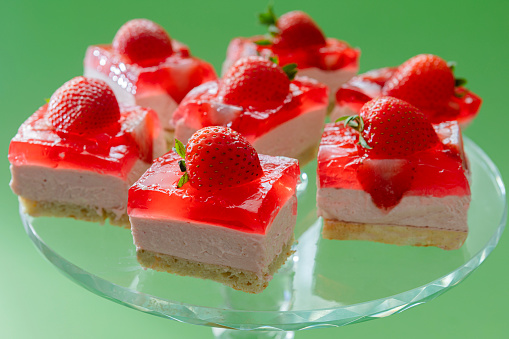 Strawberry layered desert with strawberry jelly, strawberry mousse and almond cake on a glass cake stand with a green background