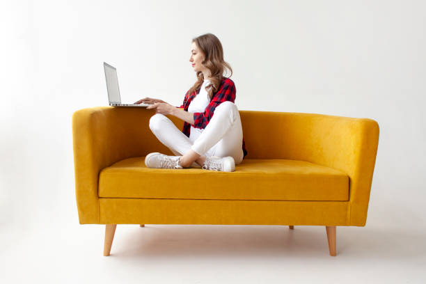 istock young cute girl uses laptop on comfortable soft sofa, woman types online on computer on yellow couch 1663010772