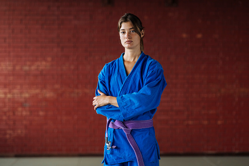 A young brunette woman in a photo poses in a blue kimono while wearing a purple belt