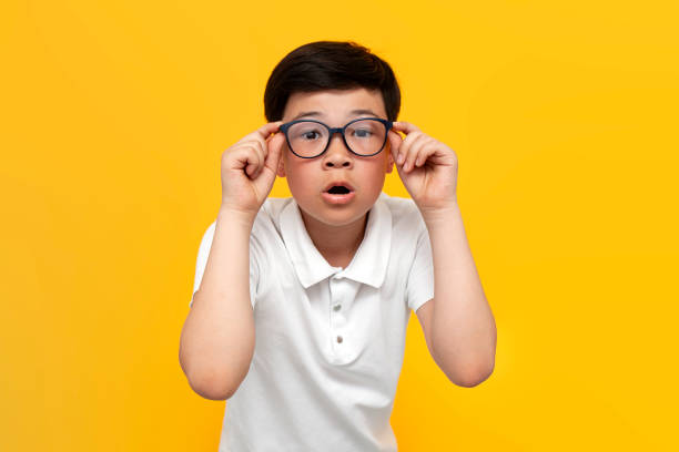10歳のショックを受けたアジアの少年は、黄色い背景に眼鏡と不思議を楽しみにしている - 10 11 years little boys glasses portrait ストックフォトと画像