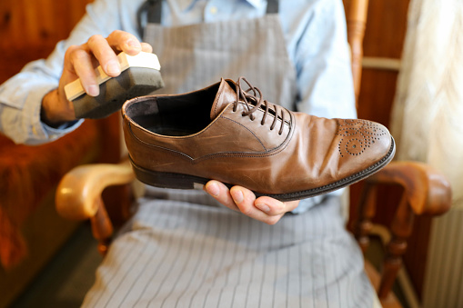 Close-up shot of man cleaning and polishing handmade brown designer shoes. The shoes are elegant and expensive.
