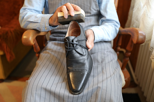 Close-up shot of a man cleaning and polishing handcrafted black designer shoes.  The shoes are elegant and expensive.