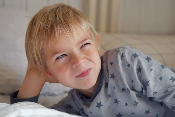 5 years Boy joking, sticking tongue out with silly expression. Child making face. Funny foolishness portrait of little boy in white bedroom. Adorable caucasian kid making crazy and comical gesture.