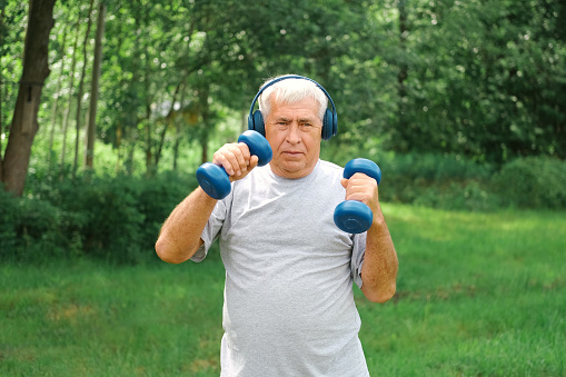 Senior man working out outdoors. Person lifting dumbbells. Old male exercising at park. Healthy people lifestyle. Active sport training. Older elderly sportsman doing fitness exercise. Workout session. Boomer. Old elderly man in sportswear training doing weight lifting dumbbell exercising. Leisure healthy lifestyle. Older male is working out. Fitness for seniors. Active retired people. Mature senior man doing gymnastics. Concept of fitness, recreation, well being, fit. Elderly male exercising training, stretching. Old man energy working out, practice. Retiree person. Sportive Grandpa pensioner on nature background. Cinematic shot. retired working out