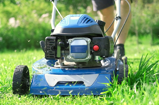 Lawn mower cutting grass. Small grass cuttings fly out of lawnmower. Grass clippings get spewed out of a mower pushed around by landscaper. Slow Motion. Close Up. Gardener working with mower machine.