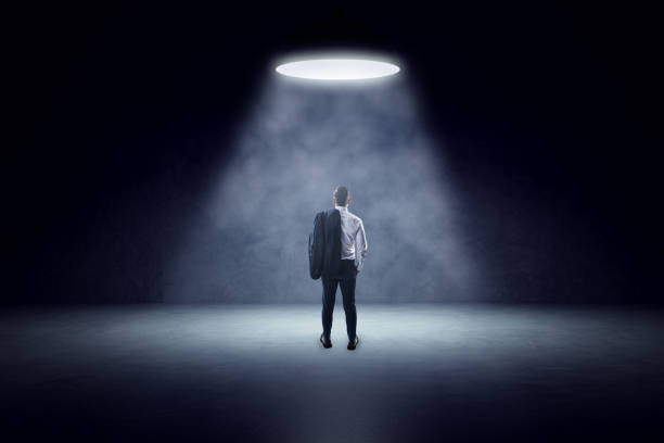istock Back view of young man standing in spotlight of lamp in concrete interior. 1663012311