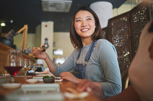 Asian, sushi and woman at a restaurant eating for dinner or lunch meal using chopsticks and feeling happy with smile. Plate, young and person enjoy Japanese cuisine, noodles or diet at a table