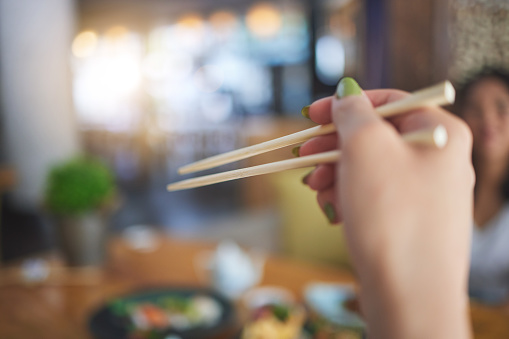 Tradition, bamboo chopsticks and hand of a person eating Japanese food at a restaurant for nutrition. Closeup of a woman with wooden sticks or utensil for dining, culture and cuisine for diet