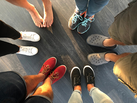 Group of young people feet stand in a circle. Five people in shoes and one barefoot