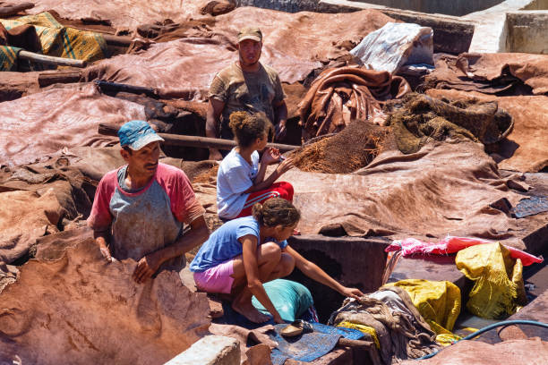 A vibrant scene of a traditional Moroccan tannery in Fes, showcasing multiple colorful vats and a laborer engaged in dyeing leather with natural processes.