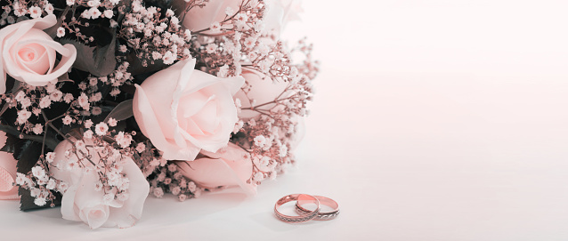 Soft focus gypsophila, rose flower bouquet and gold rings. Wedding horizontal copy space beige pink background.