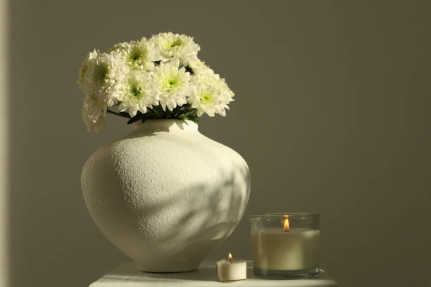 istock White chrysanthemumsand burning candle in white vase on gray interior. 1663068802