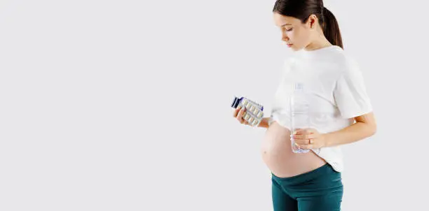 Beautiful young pregnant woman holds vitamins pills tablets in her hand and waterbottle . Pregnant Health Concept, expectation of the child, pregnancy and motherhood. High quality photo