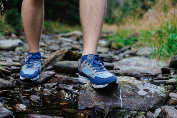 istock Crop hiker walking down stream flowing over stones in mountains 1663107538