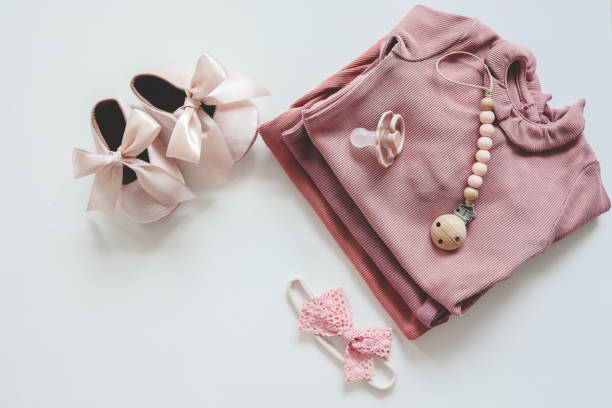 istock Stack of pink baby clothes and baby pacifier on white background 1663119026