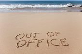 Out of office written in the sand on a beach