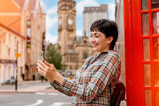 woman using phone against red phonebox traveling around English city Enjoying travel concept