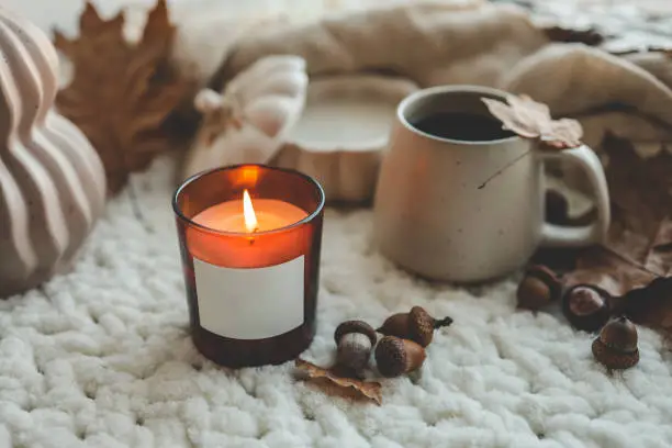 Photo of Burning candle with label isolated in autumn interior