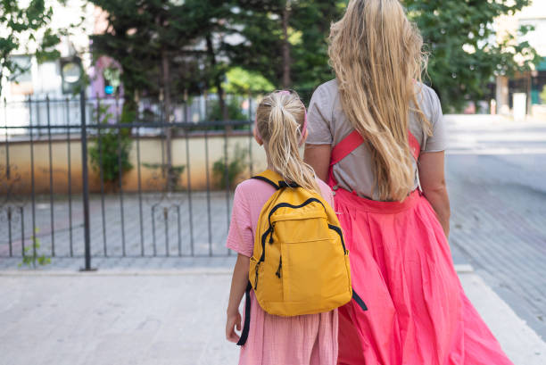 istock Mother and daughter, backpacks on, walk to school, their figures seen from behind 1663133839