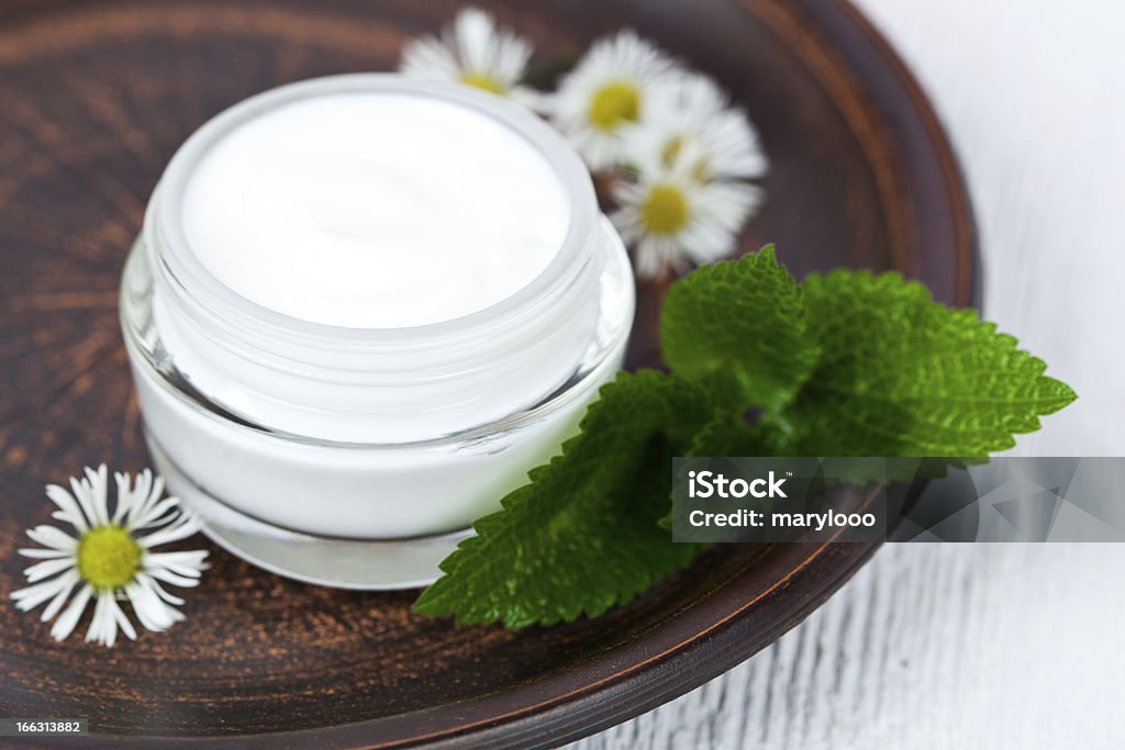 White cream on glass bottle and chamomile on a wooden plate container with cream, urtica and chamomiles on browm plate  Moisturizer Stock Photo