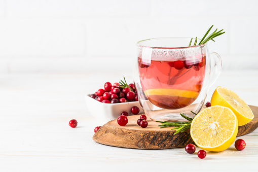 Cranberry tea with lemon and rosemary in glass mug. Healthy hot vitamin drink.