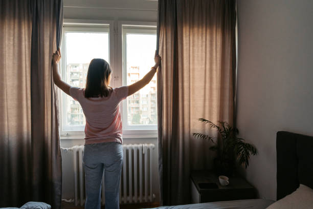 giovane donna che apre le tende nella camera da letto al mattino - dormire troppo foto e immagini stock