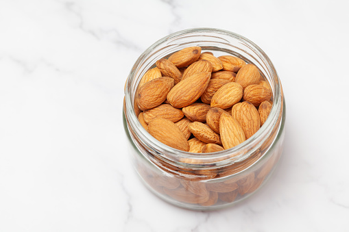 Fresh almond nuts into a glass jar isolated on marble background. Top view.