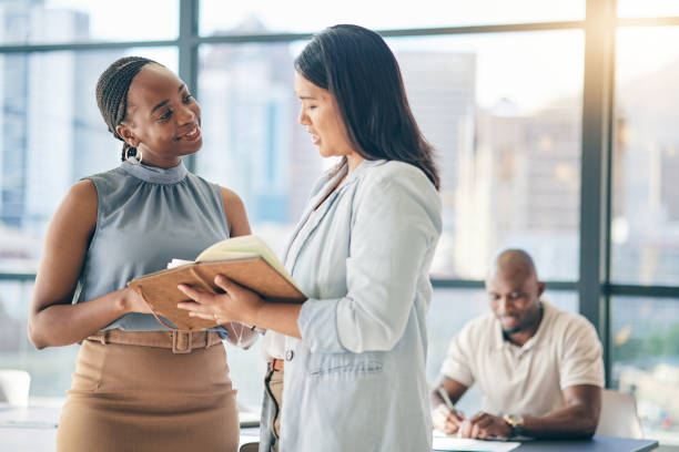 istock Collaboration, diversity and notebook with business woman planning their schedule or calendar in the office. Teamwork, agenda and a professional employee reading a journal or diary with her colleague 1663172220