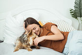A young woman is lying on the bed and playing with her dog.