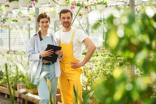 Holding tablet. Florist man and woman are working together in bright greenhouse.
