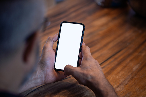 Mature man uses a smartphone with a blank white screen at the table