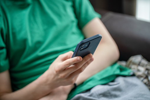 Teenage boy sits on the sofa at home and uses a smartphone