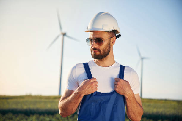 istock In blue colored uniform and in sunglasses. Service engineer is on the field with windmills 1663239897