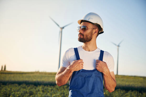 istock In blue colored uniform and in sunglasses. Service engineer is on the field with windmills 1663240437