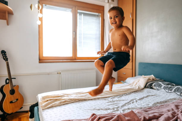 istock Cute little shirtless boy jumping on a bed in bedroom 1663245826