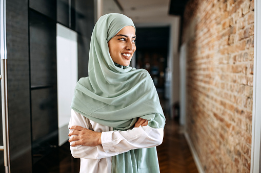 Portrait of young beautiful businesswoman wearing hijab at modern office hallway