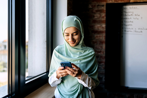 Young beautiful woman wearing hijab using phone. at modern office