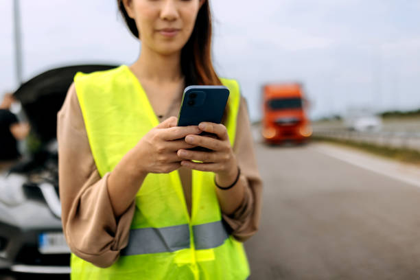 istock Young woman with reflective west text messaging for help for her broken vehicle on highway 1663257789
