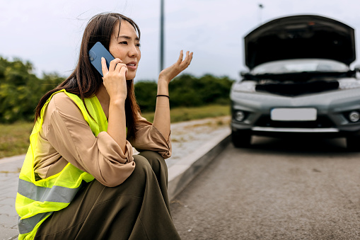 Young woman with reflective west calling help for her broken vehicle on highway