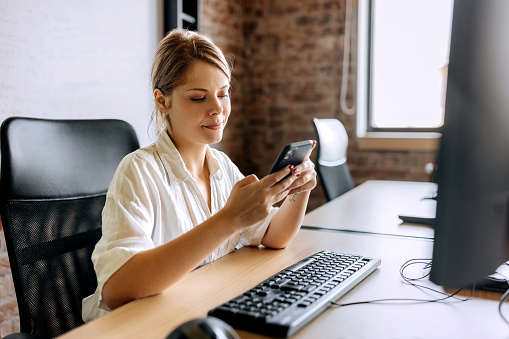 Young beautiful businesswoman using phone  while working at modern office