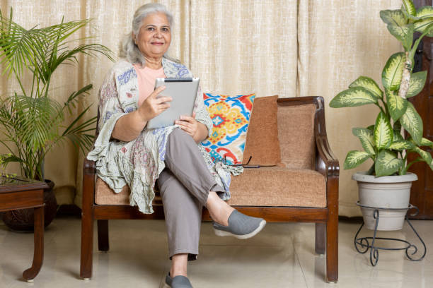 istock Resting at home. Beautiful Indian senior woman using tablet and smiling while relaxing on the couch at homeResting at home. Beautiful Indian senior woman using tablet and smiling while relaxing on the couch at home looking towards the camera 1663292301