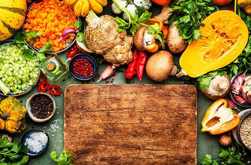 Autumn food. Vegetables, mushrooms, roots and wooden cutting board. Ingredients for vegan, vegetarian cooking. Fall harvest. Healthy diet eating, slow food concept. Rustic green table background, top view