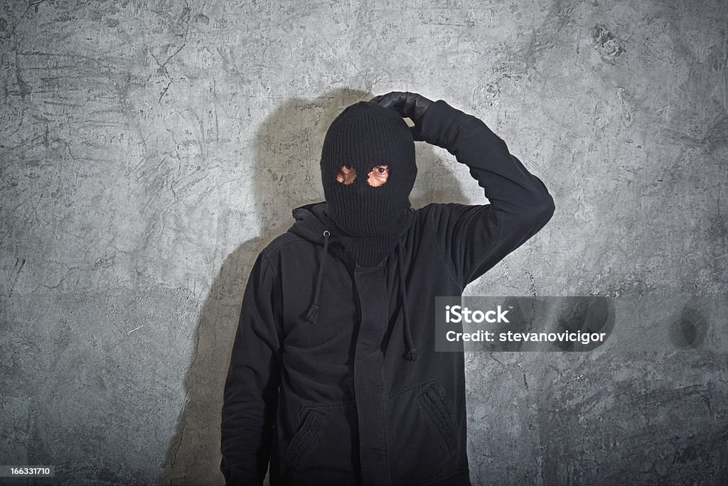 Confused burglar Confused burglar concept, thief with balaclava caught and arrested in front of the grunge concrete wall. Adult Stock Photo